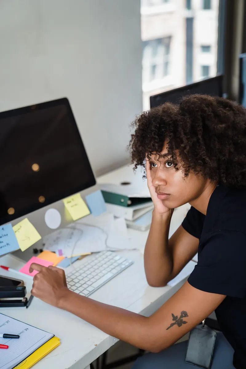 Une femme fatiguée, la tête appuyée sur la main, à son bureau